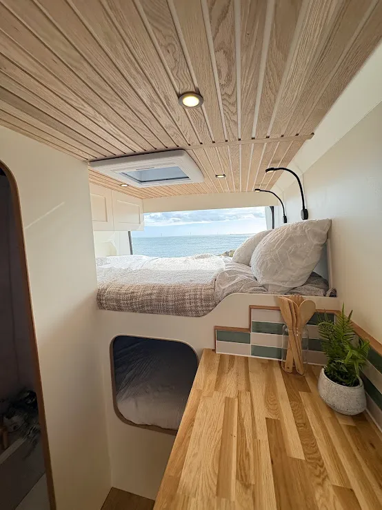 Campervan bed facing a peaceful coastal view